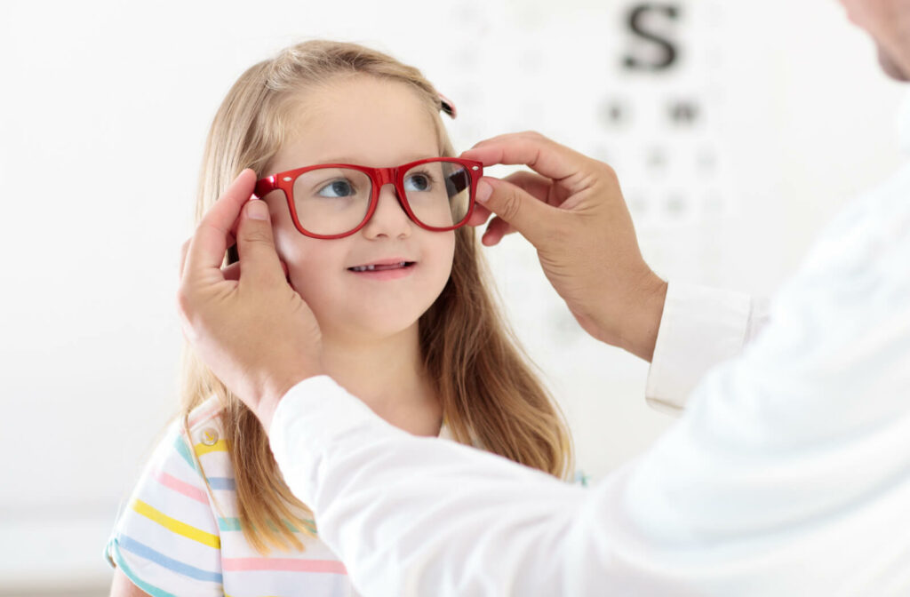 A child smiling and trying on glasses in a optical clinic while being assisted by an optometrist