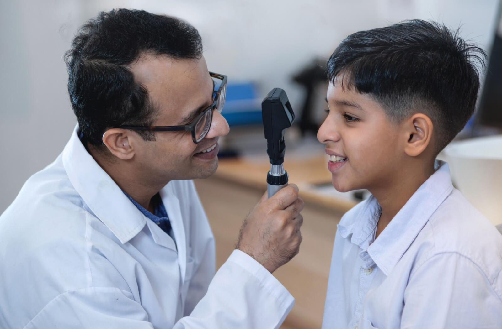 An optometrist conducts an eye exam on a young boy, both of them smiling
