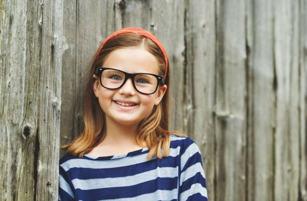 A child wearing eyeglasses outdoors, smiling and looking directly at the camera