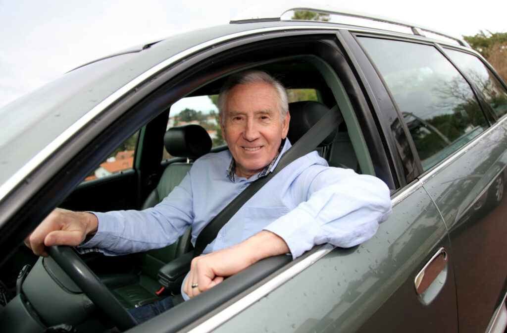 A senior man smiling and driving a car with his window open